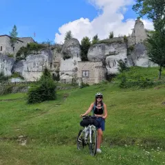 Kobieta z rowerem na tle ruin zamku na skale. Piękny dzień na odkrywanie szlak orlich gniazd rowerem.
