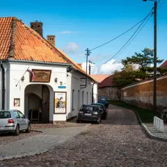 Urokliwa tykocin trasa z brukowaną uliczką, białymi budynkami i zaparkowanymi samochodami.