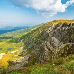 Widok na skaliste zbocze i zieloną dolinę z jeziorami. W oddali widać miasto. To krajobraz przypominający **śnieżne kotły**.