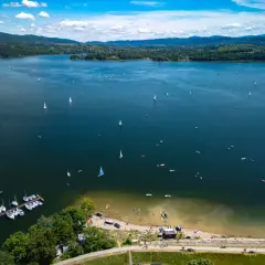 Żeglujące łodzie na błękitnym jeziorze żywieckim, z zielonymi wzgórzami w tle.