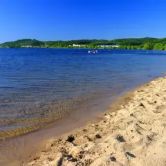 Słoneczny dzień nad Zalewem Sulejowskim. Piaszczysta plaża, błękitna woda i zielone wzgórza w tle. Idealne miejsce na relaks i wodne atrakcje.
