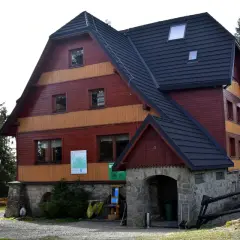 Drewniany budynek schroniska Hala Rysianka z kamiennym wejściem i znakiem "WEJŚCIE".