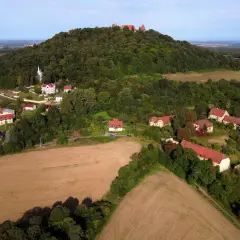 Krajobraz z ruinami zamku na wzgórzu, przypominający wygasłe wulkany w Polsce. Widać zabudowania i pola uprawne.