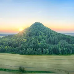 Wygasłe wulkany porośnięte lasem, otoczone polami zbóż, oświetlone wschodzącym słońcem.