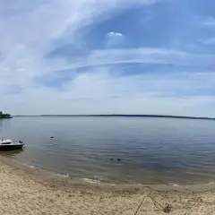 Piękny dzień nad jeziorami opolskimi. Piaszczysta plaża, spokojna woda i błękitne niebo z chmurami.