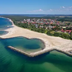Plaża w Jarosławcu, zwana "plażą Dubaj", z sercowatą zatoczką i kamiennymi falochronami. W tle widać miasteczko i las.