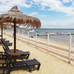 Plaża nad Jeziorem Nyskim z leżakami i parasolami. W oddali widać wodne atrakcje: łódki i rowery wodne.