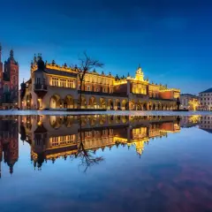 Wieczorny Rynek Główny w Krakowie z odbiciem w kałuży. Zobacz, co można robić w Krakowie: zwiedzać Sukiennice, Kościół Mariacki i podziwiać iluminacje.