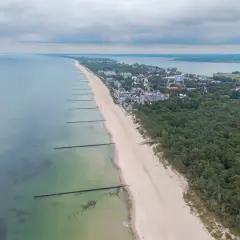 Widok z lotu ptaka na plażę w Mielnie, z falochronami i lasem sosnowym. To jedne z wielu atrakcji w Mielnie.