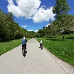 Dwie osoby na rowerach przemierzają malownicze **ojcowskie park narodowy trasy rowerowe**. Słoneczny dzień, zieleń i chmury tworzą piękną scenerię.