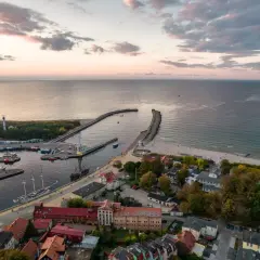 Widok na port i plażę w Ustce. Widać łodzie, latarnię morską i falochrony. To idealne miejsce na odkrywanie atrakcji Ustki i okolic.