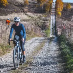 Kobieta na rowerze pokonuje kamienistą drogę w jesiennych Dolinkach Krakowskich. W tle widać innego rowerzystę.