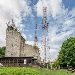 Kamienna wieża i maszty telekomunikacyjne na **chełmiec szczyt**. Ludzie odpoczywają na trawie pod drzewami.