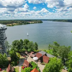 Wieża widokowa nad jeziorem Wdzydze, z której rozpościera się widok na rozległą taflę wody, żaglówkę i otaczający las.