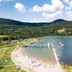 Słoneczny dzień nad zalewem Stara Morawa. Ludzie odpoczywają na plaży i w wodzie, a w tle widać zielone wzgórza.