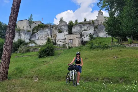 Kobieta z rowerem na tle ruin zamku na skale. Piękny dzień na odkrywanie szlak orlich gniazd rowerem.