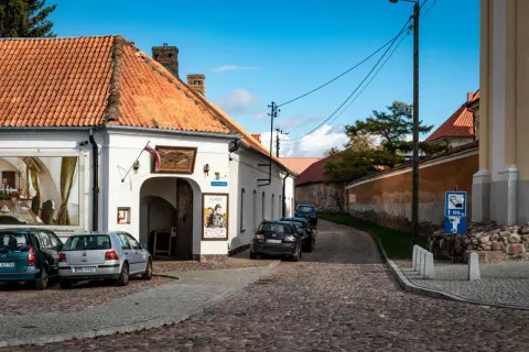 Urokliwa tykocin trasa z brukowaną uliczką, białymi budynkami i zaparkowanymi samochodami.