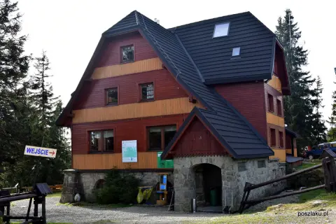 Drewniany budynek schroniska Hala Rysianka z kamiennym wejściem i znakiem "WEJŚCIE".