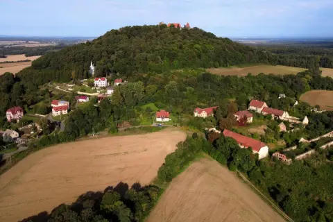 Krajobraz z ruinami zamku na wzgórzu, przypominający wygasłe wulkany w Polsce. Widać zabudowania i pola uprawne.