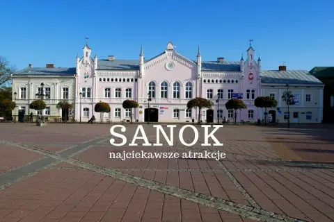 Rynek w Sanoku z pastelowymi kamieniczkami i napisem "Sanok najciekawsze atrakcje". Idealne miejsce na odkrywanie atrakcji Sanoka i okolic.