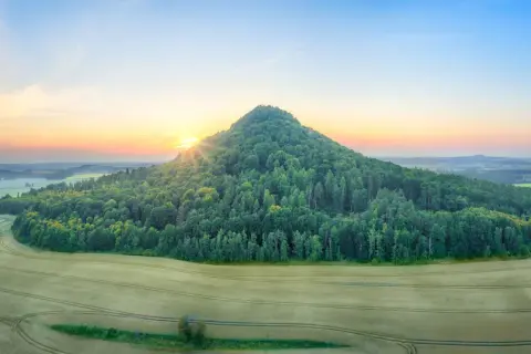 Wygasłe wulkany porośnięte lasem, otoczone polami zbóż, oświetlone wschodzącym słońcem.