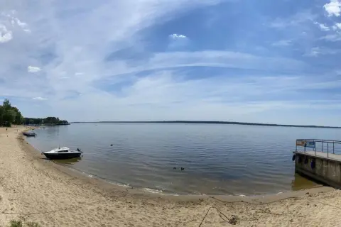 Piękny dzień nad jeziorami opolskimi. Piaszczysta plaża, spokojna woda i błękitne niebo z chmurami.