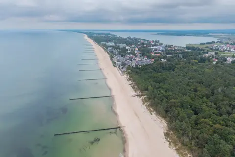 Widok z lotu ptaka na plażę w Mielnie, z falochronami i lasem sosnowym. To jedne z wielu atrakcji w Mielnie.