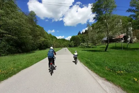 Dwie osoby na rowerach przemierzają malownicze **ojcowskie park narodowy trasy rowerowe**. Słoneczny dzień, zieleń i chmury tworzą piękną scenerię.
