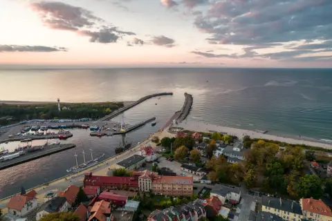 Widok na port i plażę w Ustce. Widać łodzie, latarnię morską i falochrony. To idealne miejsce na odkrywanie atrakcji Ustki i okolic.