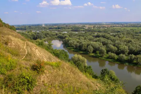 Widok na meandrującą rzekę wśród bujnej zieleni. Na pierwszym planie strome, trawiaste zbocze, przypominające krajobraz gór pieprzowych.