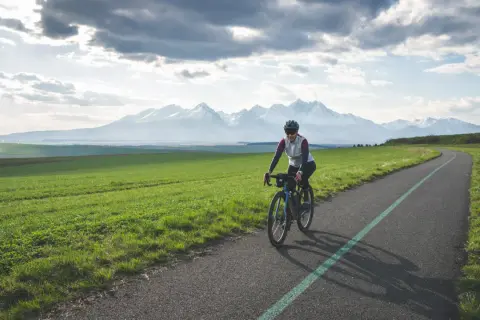 Kobieta na rowerze pokonuje malowniczą trasę z widokiem na ośnieżone Tatry. To wyzwanie: rowerem dookoła Tatr w jeden dzień!