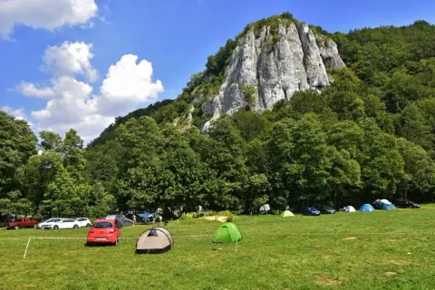 Pole namiotowe w **Dolinie Będkowskiej** pod skalistym zboczem. Turyści rozbili namioty i zaparkowali samochody na zielonej łące.