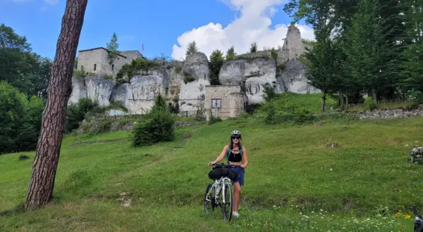 Kobieta z rowerem na tle ruin zamku na skale. Piękny dzień na odkrywanie szlak orlich gniazd rowerem.