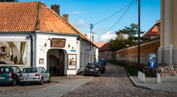 Urokliwa tykocin trasa z brukowaną uliczką, białymi budynkami i zaparkowanymi samochodami.