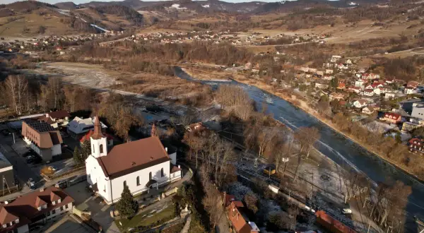 Zimowy krajobraz doliny Popradu z kościołem, rzeką i zabudowaniami.