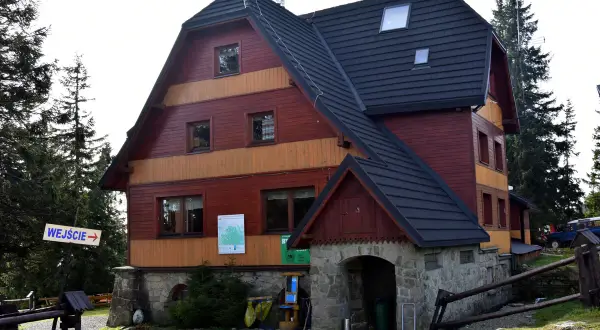 Drewniany budynek schroniska Hala Rysianka z kamiennym wejściem i znakiem "WEJŚCIE".