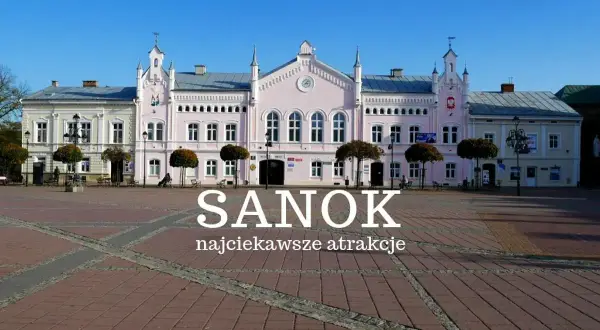 Rynek w Sanoku z pastelowymi kamieniczkami i napisem "Sanok najciekawsze atrakcje". Idealne miejsce na odkrywanie atrakcji Sanoka i okolic.