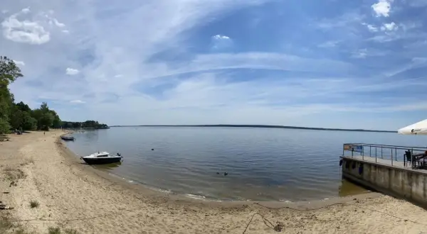 Piękny dzień nad jeziorami opolskimi. Piaszczysta plaża, spokojna woda i błękitne niebo z chmurami.