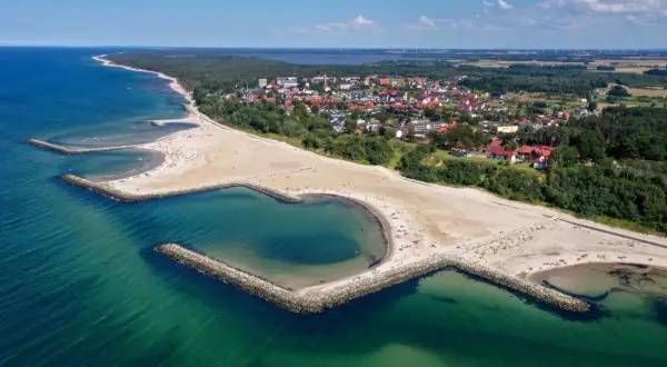 Plaża w Jarosławcu, zwana "plażą Dubaj", z sercowatą zatoczką i kamiennymi falochronami. W tle widać miasteczko i las.