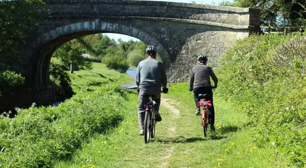 Dwie osoby na rowerach podziwiają malownicze ścieżki rowerowe lubuskie, przejeżdżając pod kamiennym mostem.