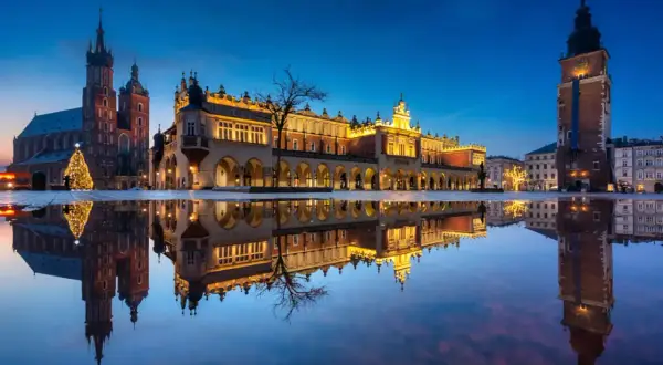 Wieczorny Rynek Główny w Krakowie z odbiciem w kałuży. Zobacz, co można robić w Krakowie: zwiedzać Sukiennice, Kościół Mariacki i podziwiać iluminacje.