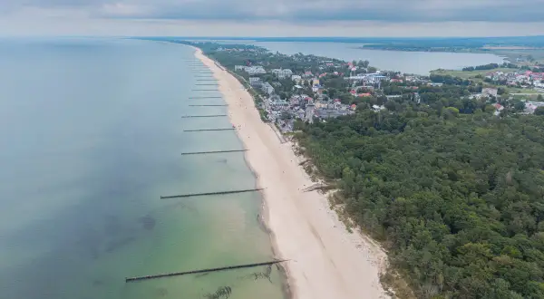 Widok z lotu ptaka na plażę w Mielnie, z falochronami i lasem sosnowym. To jedne z wielu atrakcji w Mielnie.
