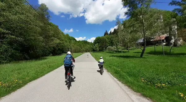 Dwie osoby na rowerach przemierzają malownicze **ojcowskie park narodowy trasy rowerowe**. Słoneczny dzień, zieleń i chmury tworzą piękną scenerię.