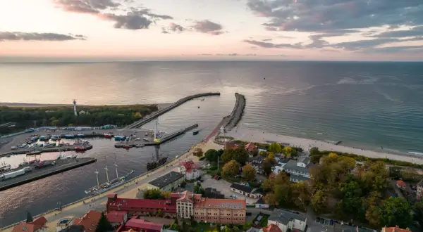 Widok na port i plażę w Ustce. Widać łodzie, latarnię morską i falochrony. To idealne miejsce na odkrywanie atrakcji Ustki i okolic.