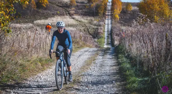 Kobieta na rowerze pokonuje kamienistą drogę w jesiennych Dolinkach Krakowskich. W tle widać innego rowerzystę.