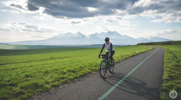 Kobieta na rowerze pokonuje malowniczą trasę z widokiem na ośnieżone Tatry. To wyzwanie: rowerem dookoła Tatr w jeden dzień!