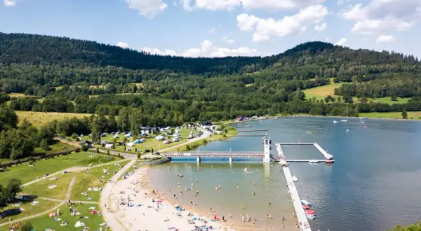 Słoneczny dzień nad zalewem Stara Morawa. Ludzie odpoczywają na plaży i w wodzie, a w tle widać zielone wzgórza.
