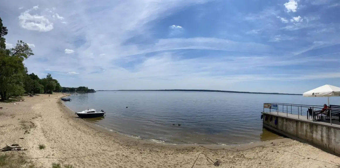 Piękny dzień nad jeziorami opolskimi. Piaszczysta plaża, spokojna woda i błękitne niebo z chmurami.