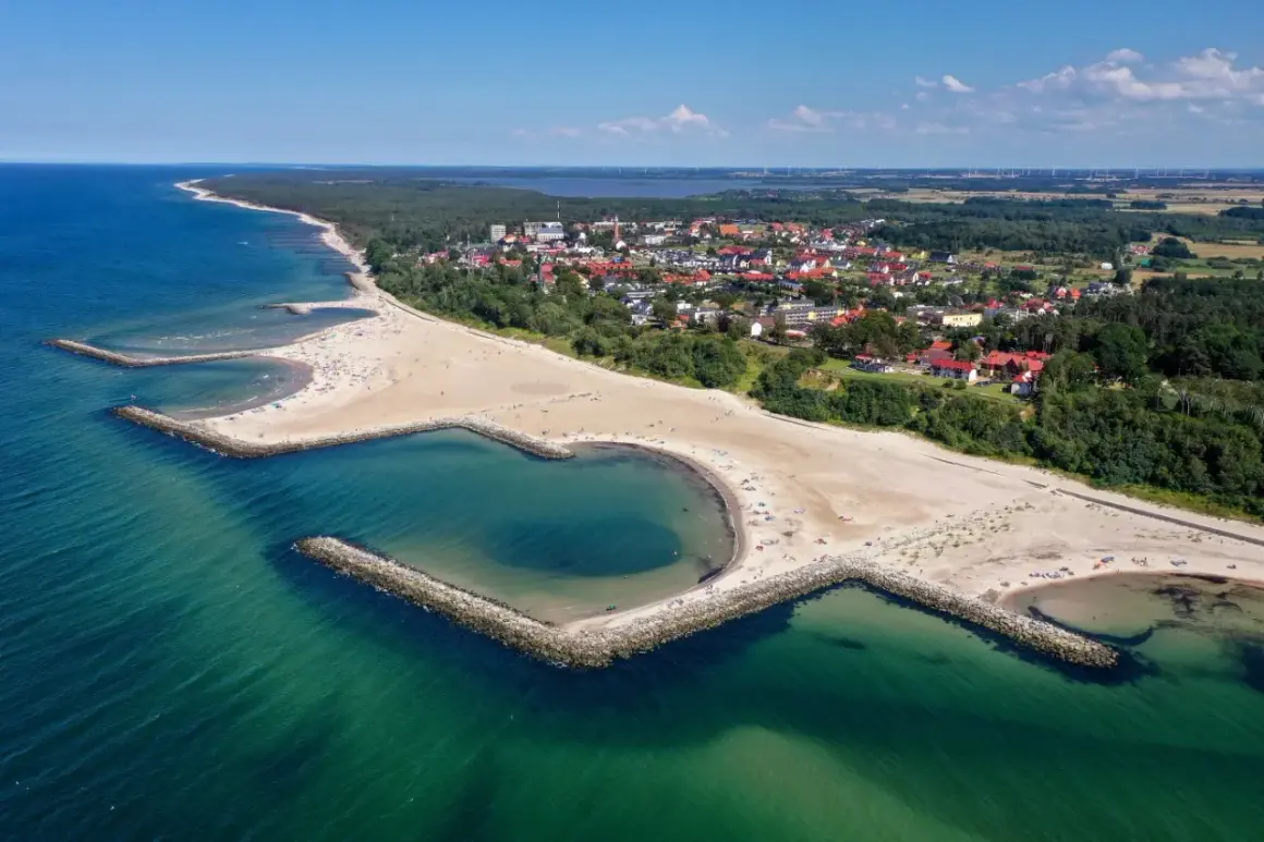 Plaża w Jarosławcu, zwana "plażą Dubaj", z sercowatą zatoczką i kamiennymi falochronami. W tle widać miasteczko i las.