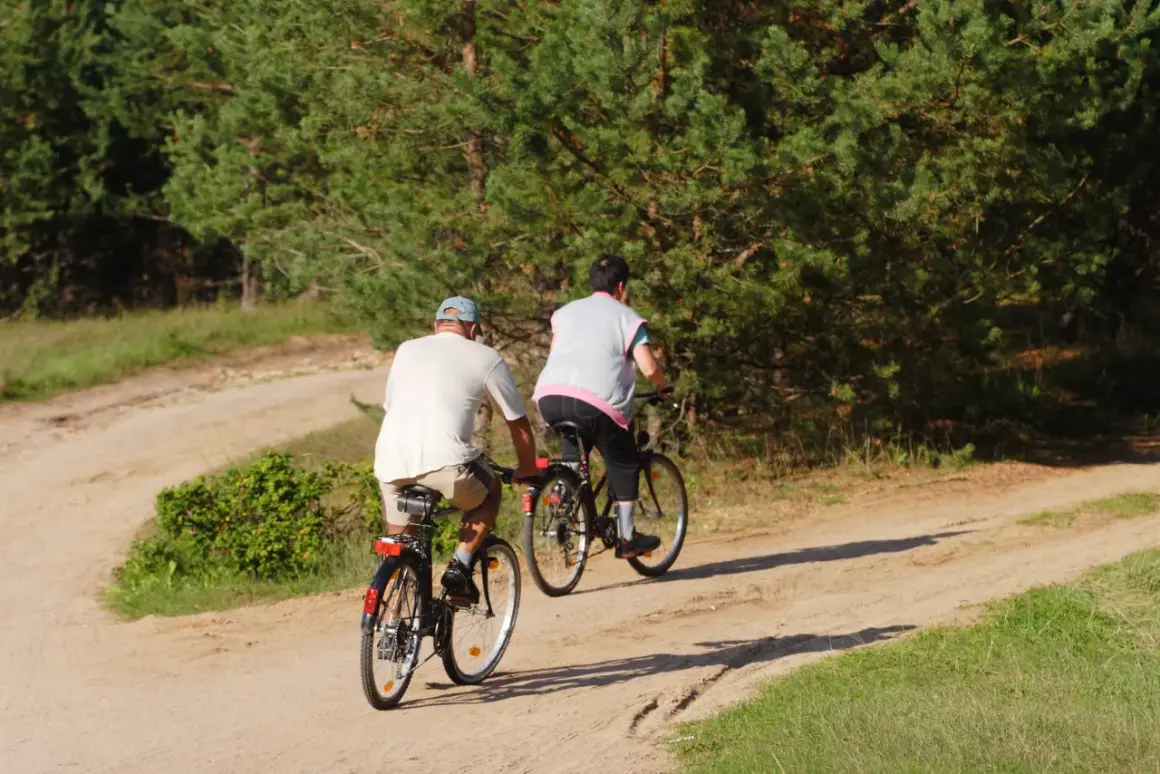 Dwie osoby na rowerach odkrywają najładniejsze trasy rowerowe na Mazowszu, jadąc piaszczystą drogą wśród drzew.